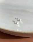 Tiny handmade sterling silver circle studs sitting on a white jewelry dish
