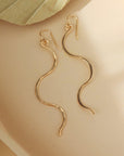 14k gold fill Sidewinder earrings placed on a tan plate. These sidewinders feature a snake like look to them with a hook earring.
