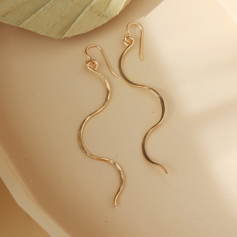 14k gold fill Sidewinder earrings placed on a tan plate. These sidewinders feature a snake like look to them with a hook earring.