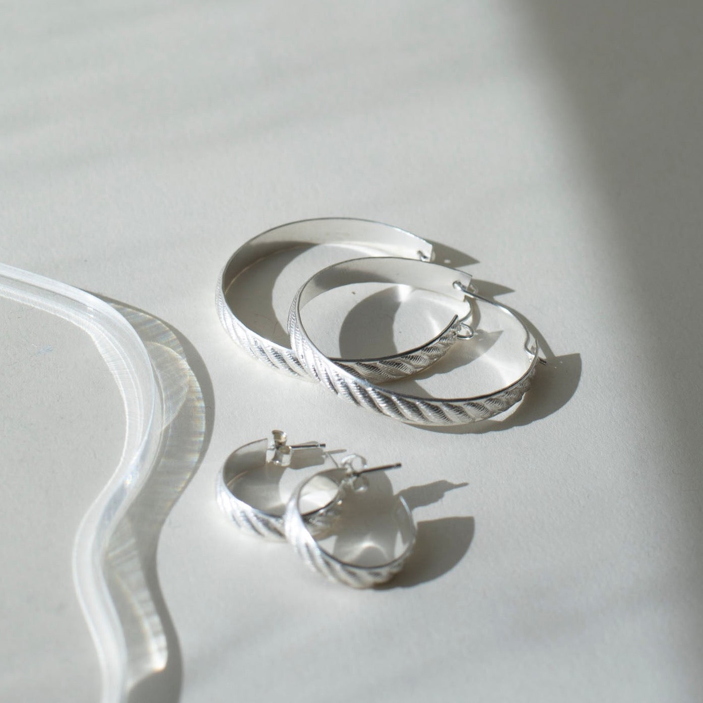 925 sterling silver hoop earrings, approximately 1.5&quot; diameter with a soft ripple pattern engraved. they&#39;re photographed on a white table in the sunlight next to the little ripple hoops