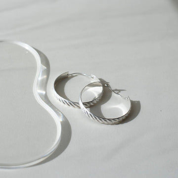 925 sterling silver hoop earrings, approximately 1.5" diameter with a soft ripple pattern engraved. they're photographed on a white table in the sunlight
